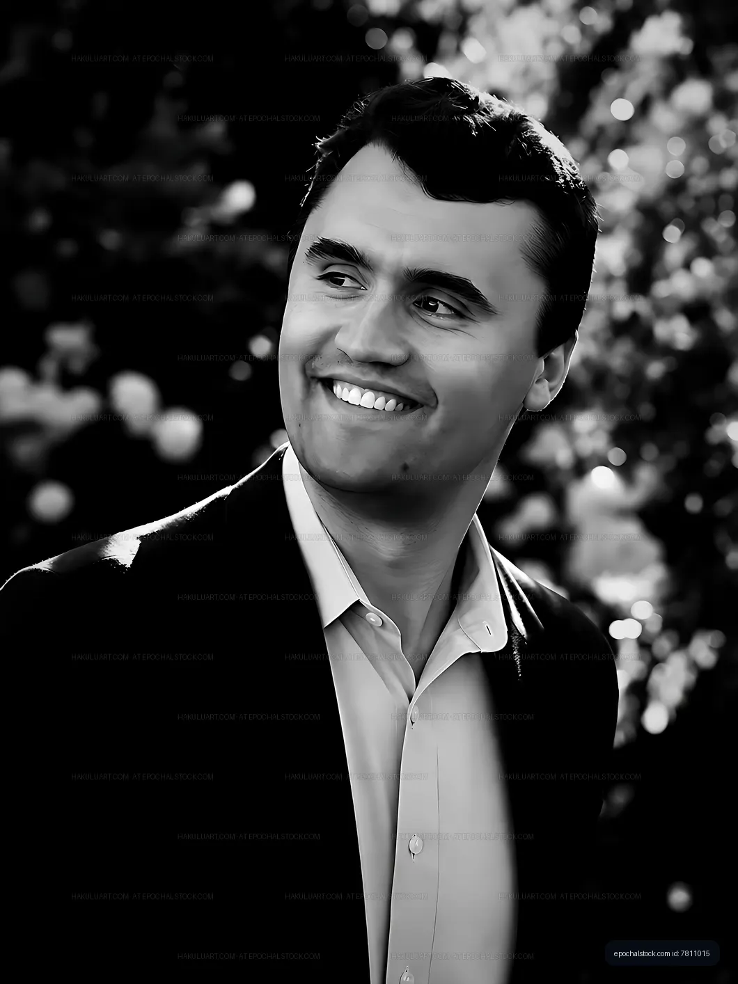 Man smiling in formal attire with blurred flowers in background