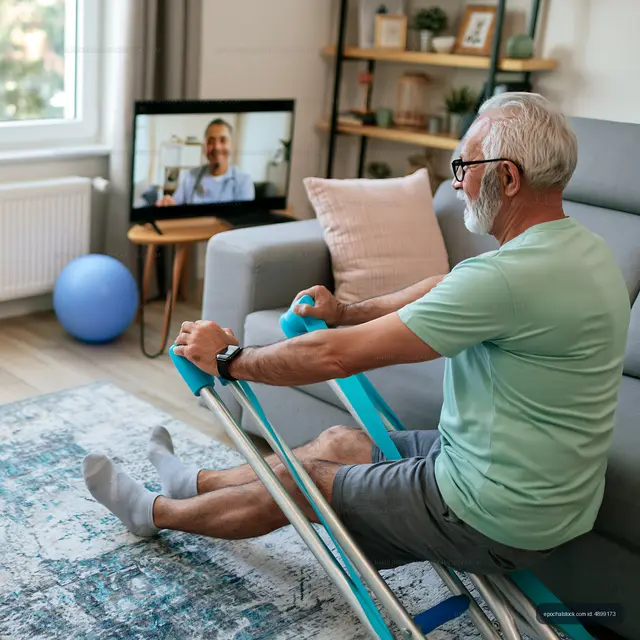 Senior man exercising at home while video calling with a trainer